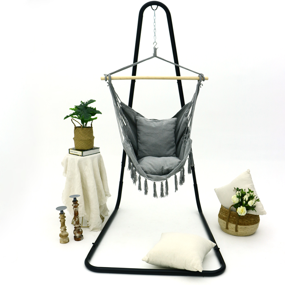 Gray double macrame hanging chair with pillows suspended outdoors, showcasing the solid wood spreader bar and intricate cotton woven structure
